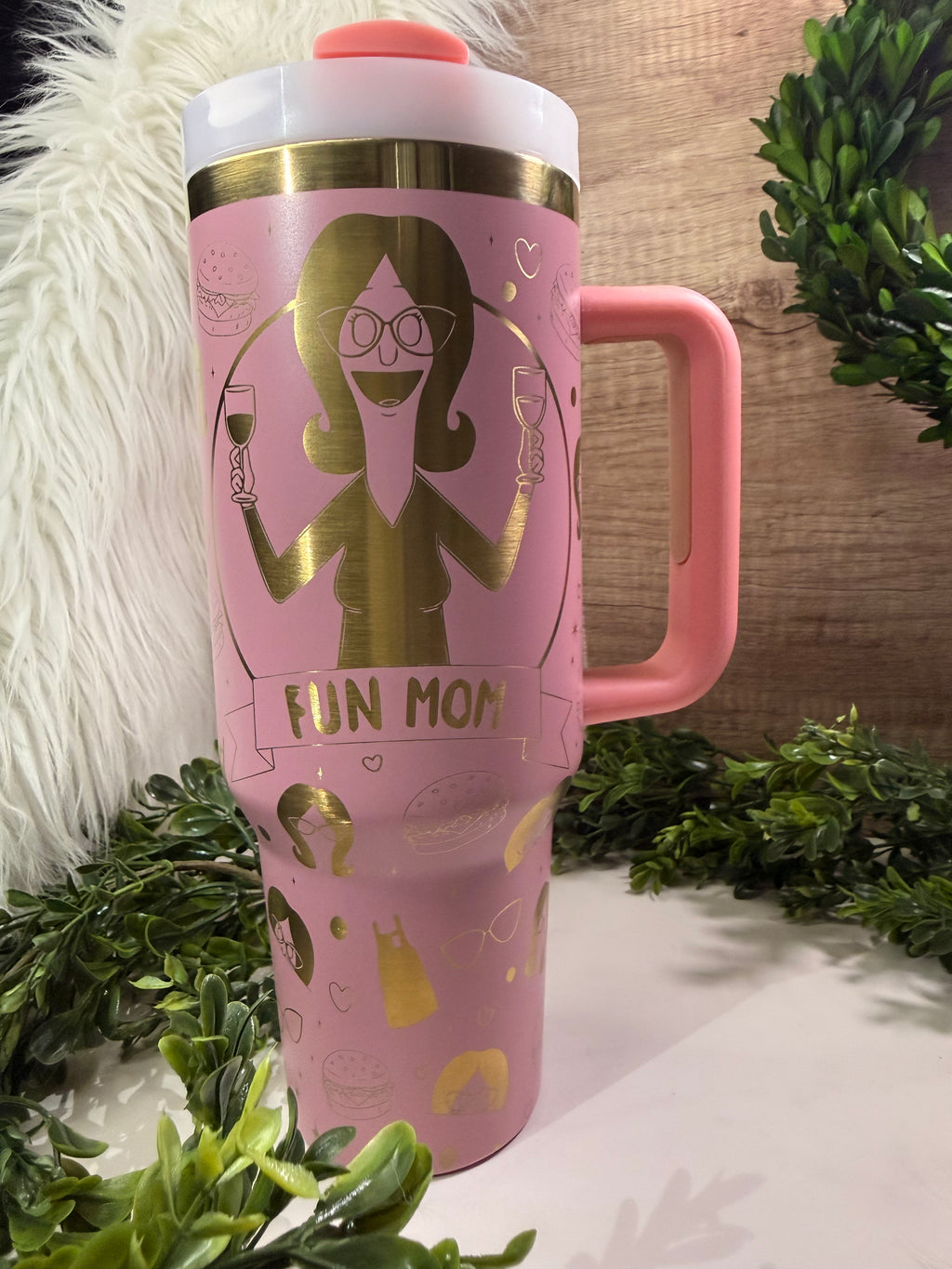 Pink travel mug with a graphic of Linda belcher and 'FUN MOM' text, surrounded aprons, burgers, glasses